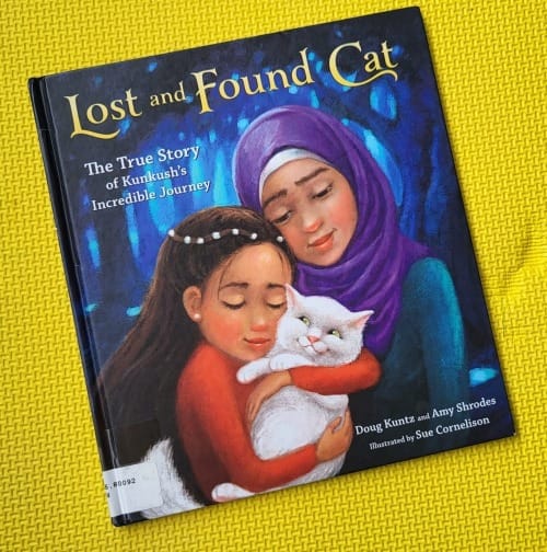 The cover of the picture book Lost and Found Cat features a lovely illustration of a young girl with flowing brown hair cradling a smiling white cat. A woman stands beside them, looking down at both with love.
